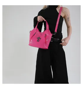 Detail of bright pink leather crossbody bag with gothic metal cross charm and zippers