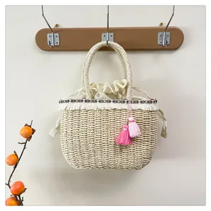 Dettaglio di borsa in paglia con nappe boho e fodera con coulisse su un gancio in legno