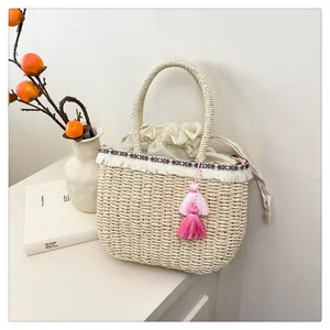 Dettaglio della borsa in paglia beige con nastro geometrico e nappa rosa chic