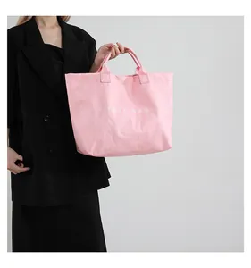 Detail of soft pink oversized tote bag with TOTE BAG print held by a model in a suit
