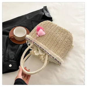 Dettaglio della borsa in paglia intrecciata con nappe rosa e bordo geometrico boho