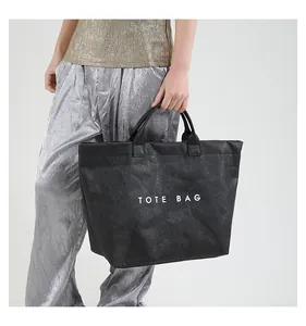 Detail view of large matte black tote bag with crushed paper texture and printed text