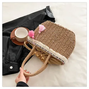 Dettaglio borsa in paglia intrecciata con nappe rosa e nastro geometrico decorativo
