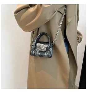 Close-up of mini metallic crossbody bag with skull embossing and silver chain strap