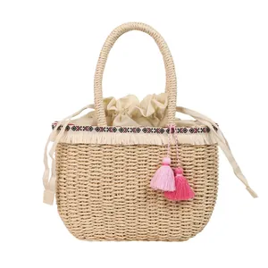 Borsa tote estiva in paglia con nastro etnico e nappe rosa su sfondo bianco