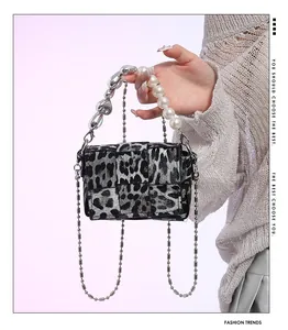Detail of leopard print handbag with pearl handle, heart charm, and woven texture