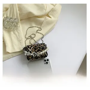 Detailed view of leopard print crossbody bag with heart-pearl chain next to a smartphone