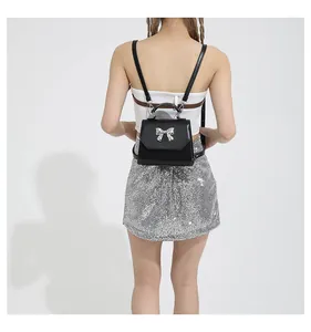 Detail of a mini black flap bag with a silver bow ornament on a silver sequin dress model