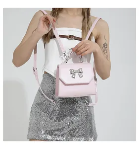 Detail of pink faux leather bag featuring a silver metal bow and adjustable strap