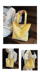 Detail of yellow canvas tote bag showing white heart embroidery and small metal heart buckle
