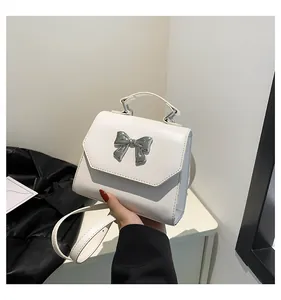 Close-up of a white leather crossbody bag with a silver metallic bow and top handle