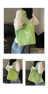 Detail view of the green canvas tote bag featuring an embroidered white heart and metal ornament