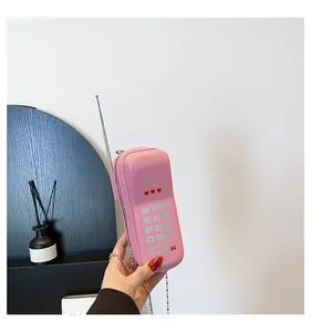 Détail d'un sac bandoulière rose en forme de téléphone rétro avec chaîne en métal