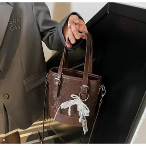 Detail der dunkelbraunen Eimer-Tasche mit Schlangenprägung und Spitzen-Anhänger