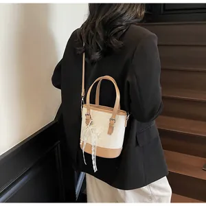 Spitzenschleife und Perlendetail an einer weißen Eimertasche mit braunen Lederriemen