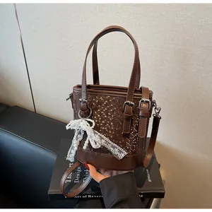 Detailansicht der braunen Beuteltasche mit Schlangenhaut-Prägung und Perlen-Spitzenschleife