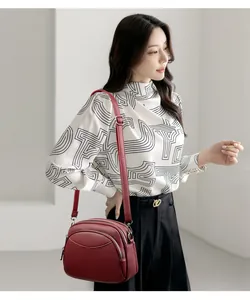 Detail of burgundy lychee grain leather crossbody bag with multiple zipper compartments