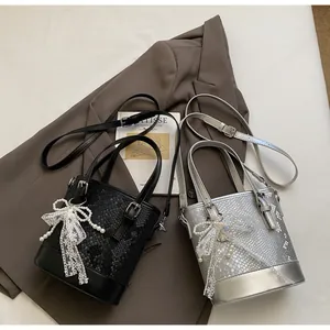 Detail der silbernen Eimertasche mit Schlangenprägung, weißer Spitzenschleife und Perlenanhänger