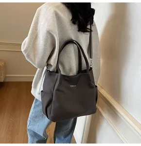 Vista laterale di una borsa tote in tela scura indossata da una modella in interni