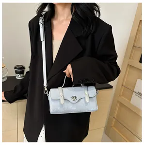 Close-up of a light blue textured crossbody bag with silver twist lock on black suit