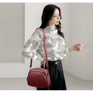 Chic burgundy leather crossbody round bag with dual zippers and adjustable shoulder strap