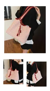 Close-up of red and white striped canvas tote with premium leather trim and charm detail