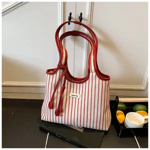 Detail of large striped canvas tote with red leather handles and tassel ornament