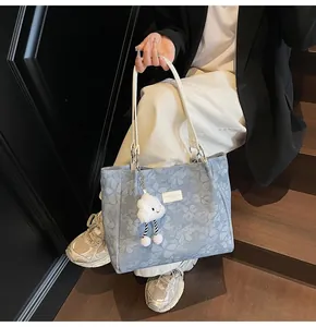 Detail of light blue floral tote bag with white leather tag and cloud plush charm