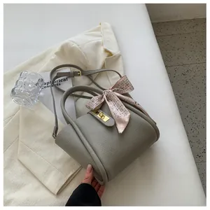 Détail du sac seau en cuir gris avec foulard en soie rose et fermoir doré rotatif
