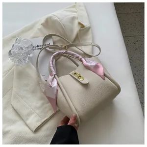 Détail d'un sac seau crème en cuir avec poignée ornée d'un foulard en soie rose