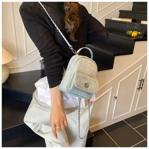 Detail of light blue denim mini backpack with silver twist lock and metal chain strap