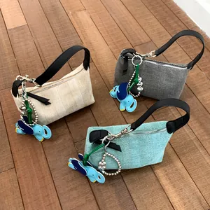 Three woven fabric tote bags in beige, grey, and blue with leather straps and elephant charms