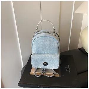Detail of light blue washed denim backpack with silver metal twist lock and chain strap