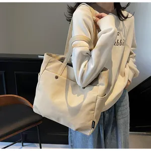Detail of the beige canvas tote bag showing the wide strap and front button pocket