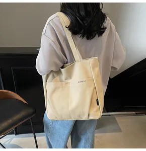Detailed view of beige canvas tote bag with front pocket and Midolai logo on model
