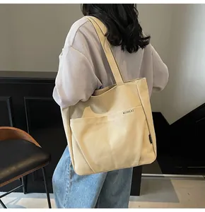 Detail of minimalist beige canvas tote bag showing two front pockets and side brand label