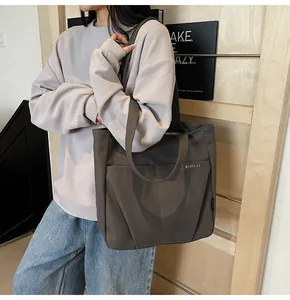 Detail of dark brown canvas tote bag with front pocket shown on shoulder with casual outfit
