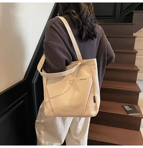 Detail of beige canvas tote bag showing outer pocket and MIDOLAI branding on a shoulder strap