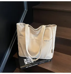 Detail of off-white canvas tote bag featuring front pocket and minimalist brand logo