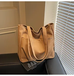 Detail of canvas tote bag showing IDOLAI embroidery and front pocket on a minimal setting