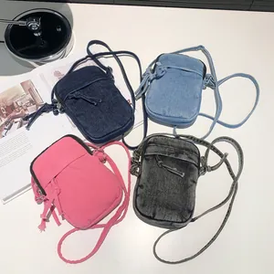 Mini washed denim crossbody bags in four colors with zipper and knot detail on white table