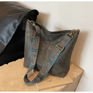 Detail of grey suede tote bag with a wide colorful woven strap and golden hardware