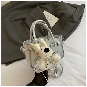 Détail du sac à main argenté métallisé avec une breloque d'ours en peluche blanc