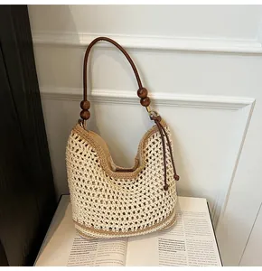 Close-up of woven hobo bag with brown leather handle and decorative dark wood beads