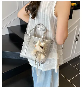 Silberne Eimer-Tasche mit Krokodil-Prägung und Plüsch-Anhänger an einem Modell