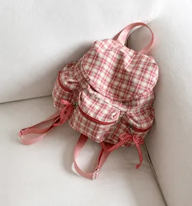 Detail of pink plaid canvas backpack showing multiple zip pockets and red bow charms