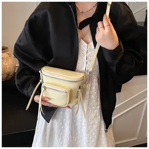 Gros plan d'un sac bandoulière crème avec fermetures éclair argentées et tirettes en cuir