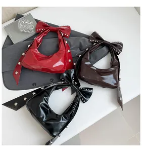 Detail von glänzenden Schleifenhandtaschen in Rot, Kaffee und Schwarz mit Nietenbesatz
