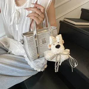 Silberne Glitzer Eimertasche mit Wellenstruktur und weißem Bär-Anhänger, von Model gehalten