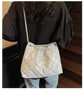 Détail du sac seau matelassé crème avec rivets, emblème étoile et bandoulière sur mannequin